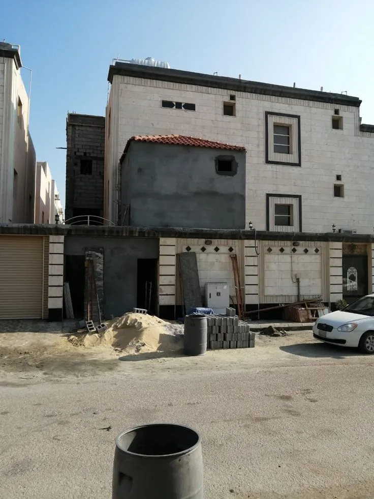 صورة لمبنى سكني أثناء أعمال ترميم وتوسعة في المدينة المنورة، يظهر فيها الجدار قيد التشطيب ومواد البناء مثل الرمل والطوب أمام المبنى