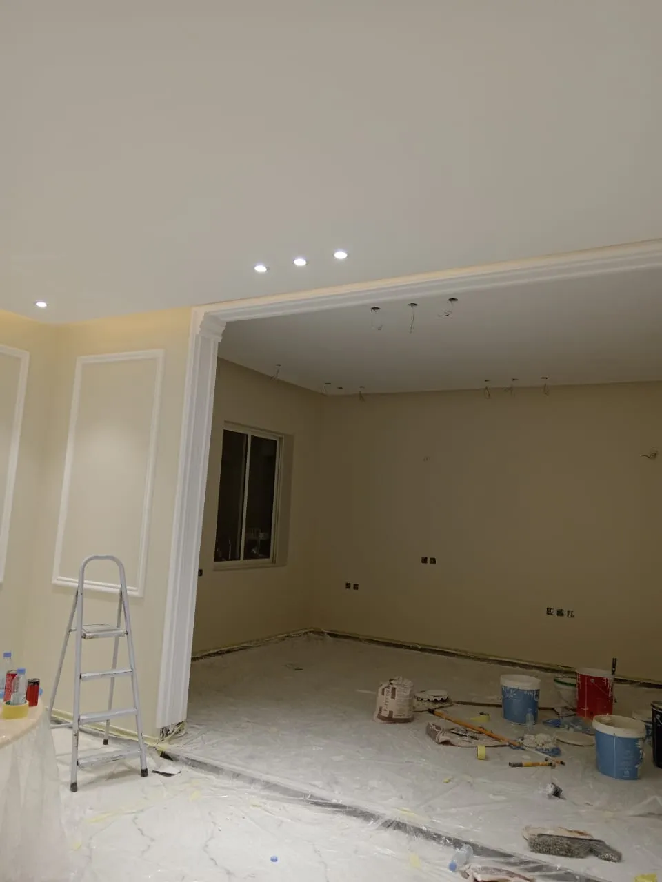 غرفة قيد التشطيب في المدينة المنورة، تظهر فيها أدوات الدهان والسلالم مع جدران بلون بيج وإضاءة سقف